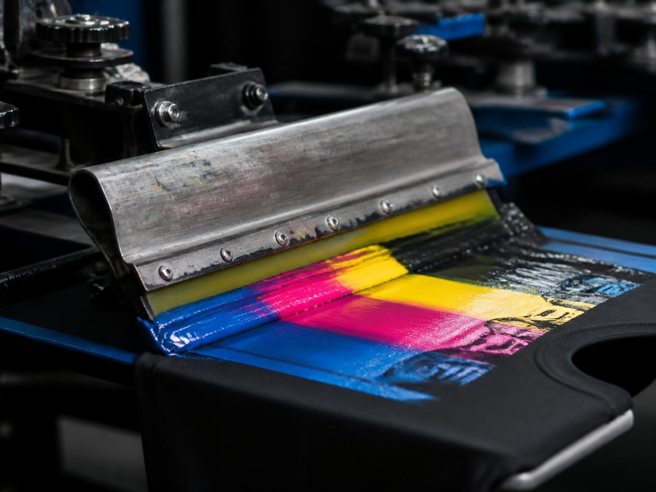 CMYK screen printing squeegee pulling ink across a black t-shirt